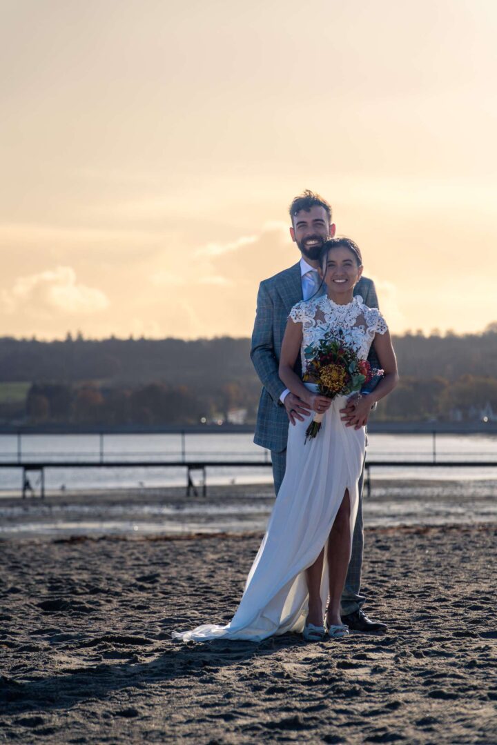 Couple standing close on the beach, smiling at the camera, radiating love and happiness.