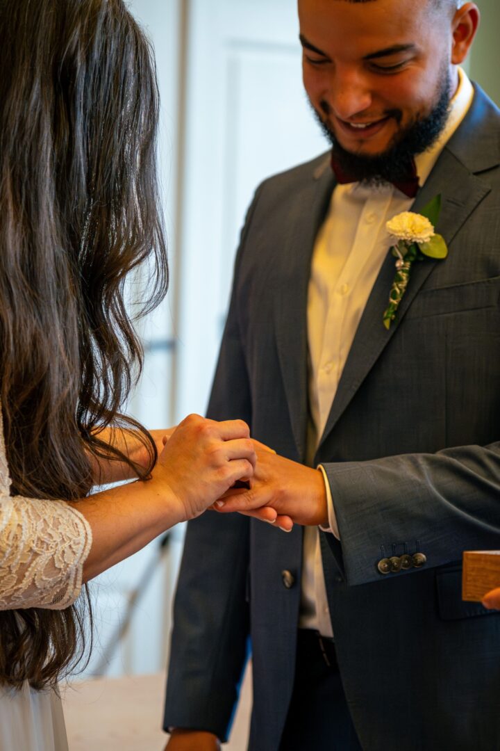 Bride putting the ring on the groom’s finger in the town hall, both smiling at the special moment.