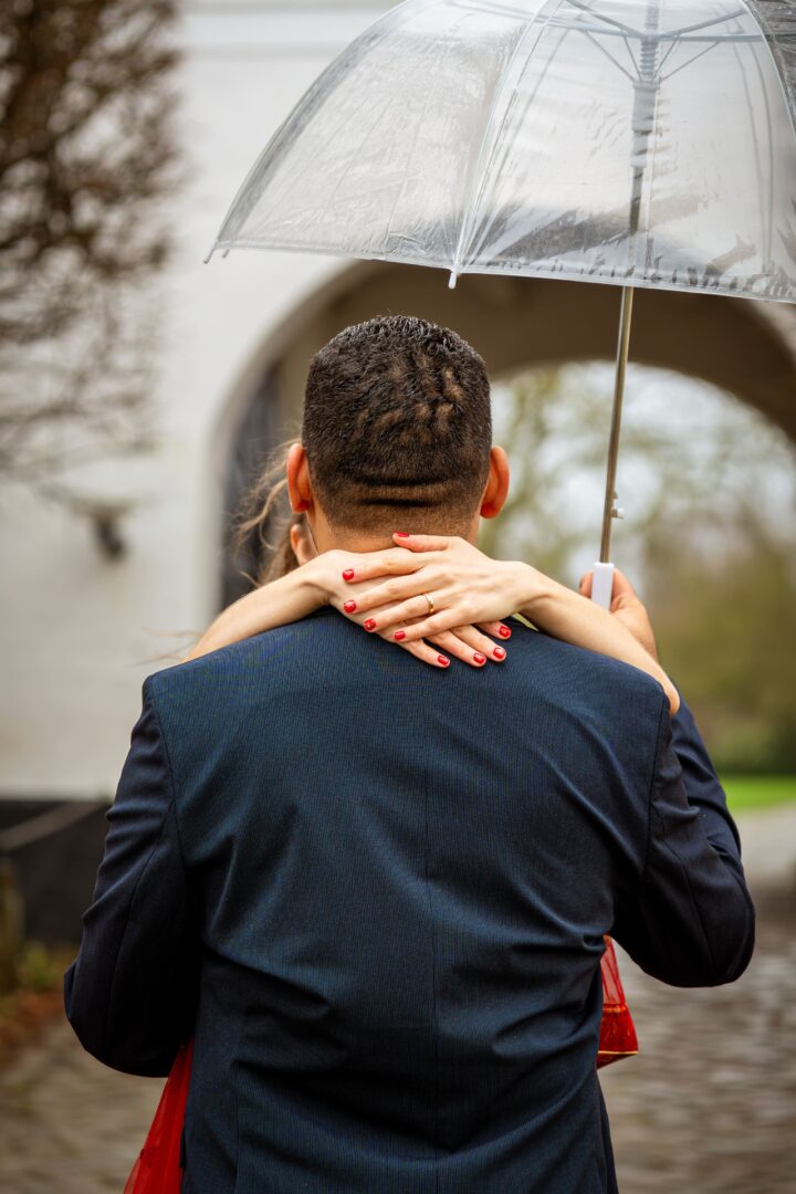 Bride hugging the groom at Brundlund Castle in the rain as he holds an umbrella, creating a romantic and timeless moment.