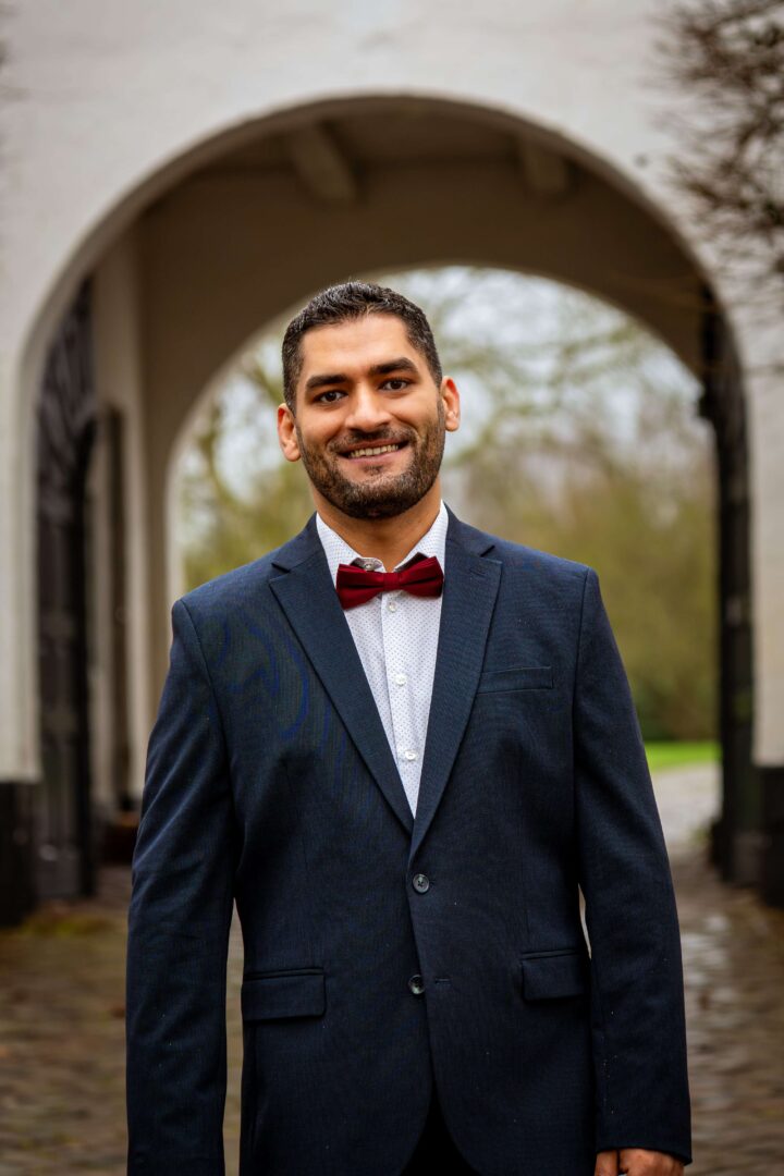 Portrait shot of the groom in a bow tie and suit, standing confidently in front of the Brundlund Castle entrance.