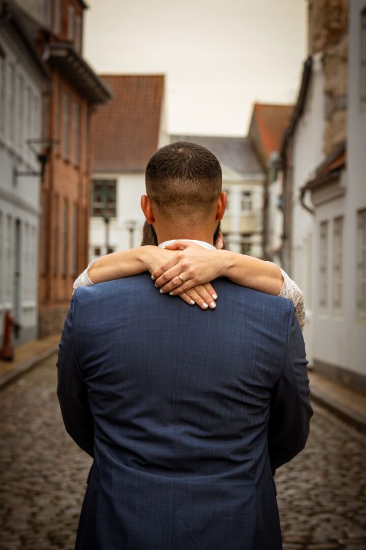 Bride holding her groom from behind, with the wedding ring visible as they stand together in a beautiful setting.