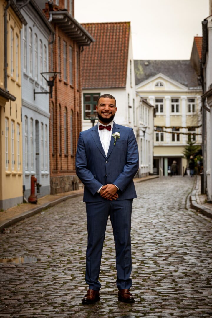 Full-body portrait of the groom standing in a charming old street, smiling with confidence and joy.