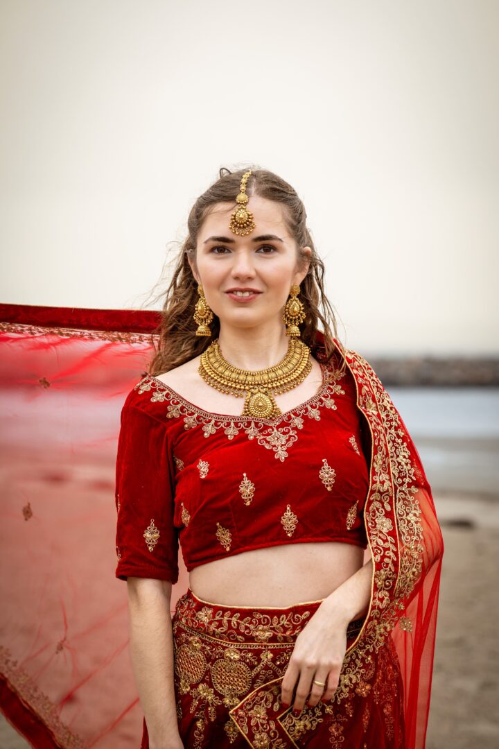 Bride at the beach wearing Nepalese traditional clothes, with a subtle smile as she looks at the camera.