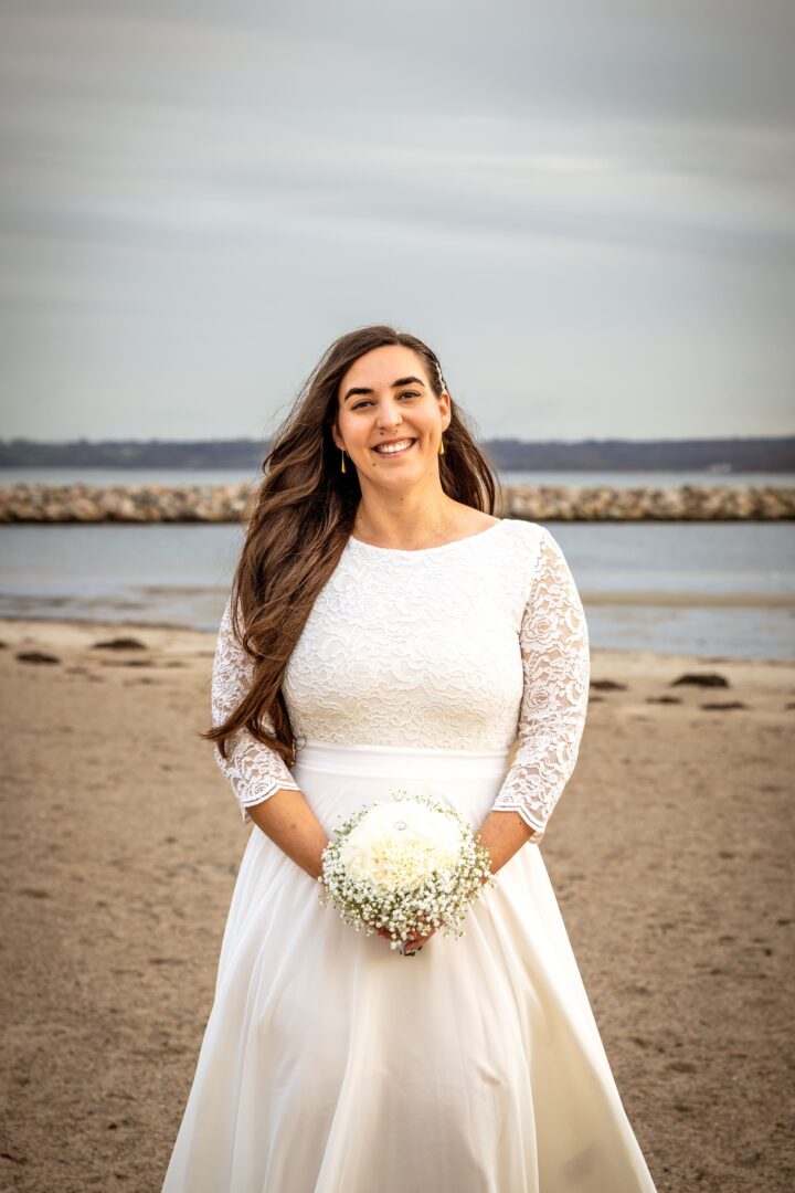 Knees-up shot of the bride smiling on the beach, holding her beautiful flower bouquet.