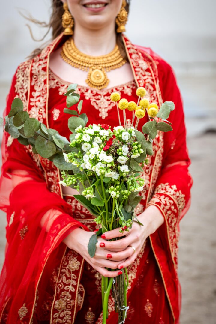 Woman in a red traditional dress holding a simple bouquet of flowers, captured in a beautiful moment.