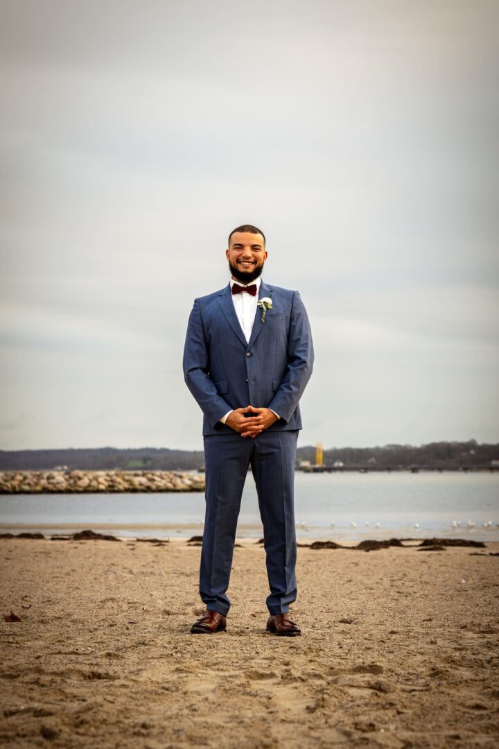 Full-body portrait of the groom standing on the beach, with a relaxed and joyful expression.