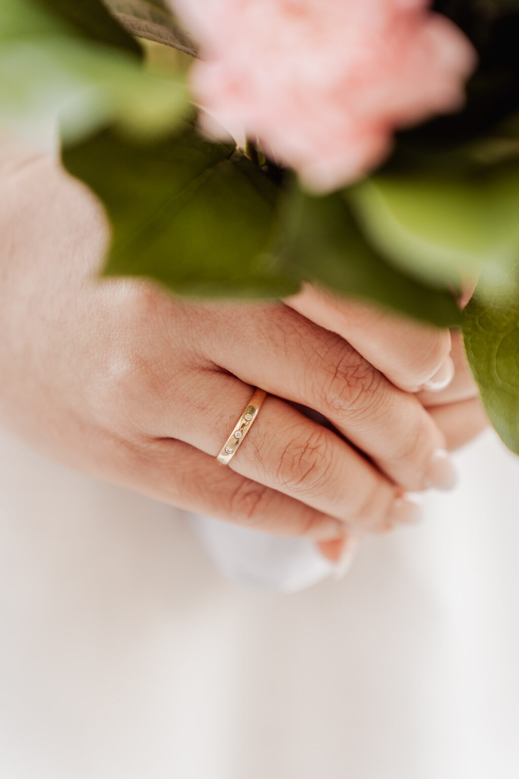 The bride rests her hands on her bouquet, the gold wedding band catching the light