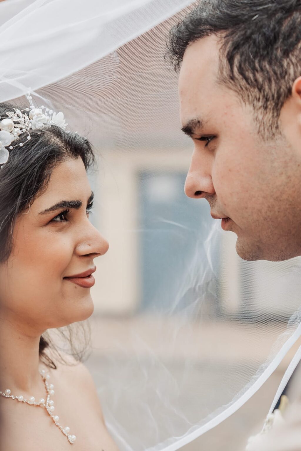 Close-up of the couple under the veil, standing close and gazing deeply into each other’s eyes.