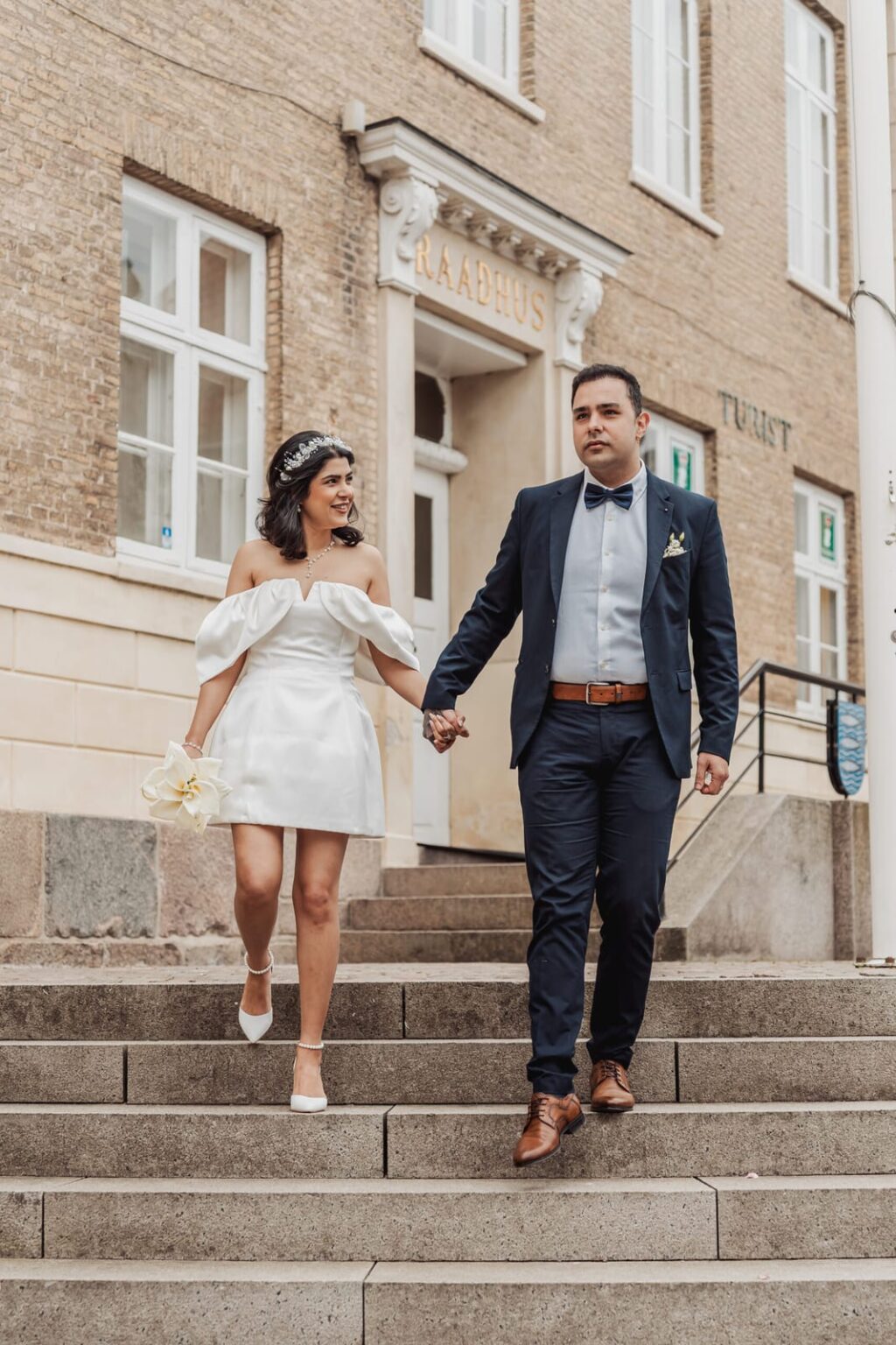 Newlyweds walking down the stairs of Aabenraa Town Hall, he looks thoughtfully ahead while she smiles at him lovingly.