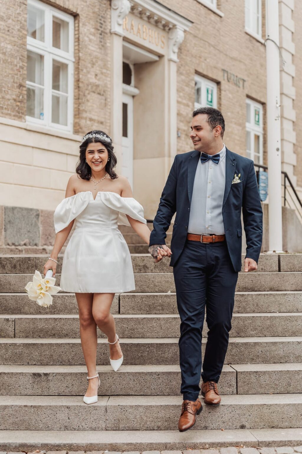 Newlyweds laughing together while walking down the stairs of Aabenraa Town Hall, his eyes warmly on her.