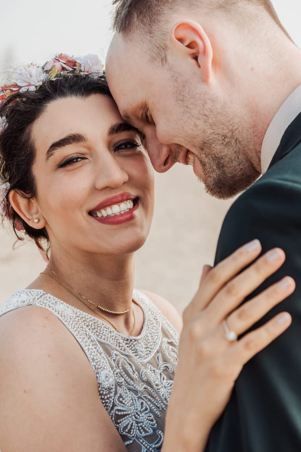 Sweet close-up of the couple touching foreheads on the beach, with the bride smiling genuinely at the camera.