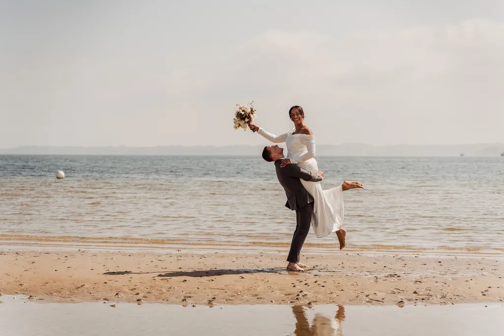 groom lifting bride on the beach after their wedding in Denmark