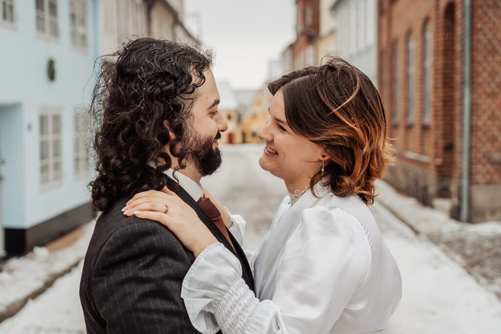 Couple facing each other in a snow covered street of pastel townhouses on their wedding day.