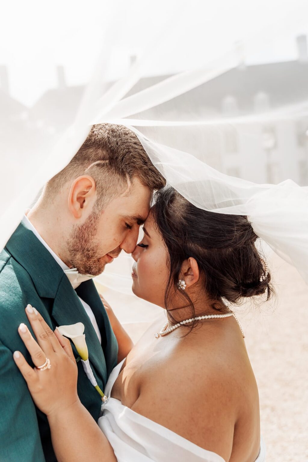 Bride and groom resting their foreheads together beneath her veil, Schackenborg Castle behind them in summer light.