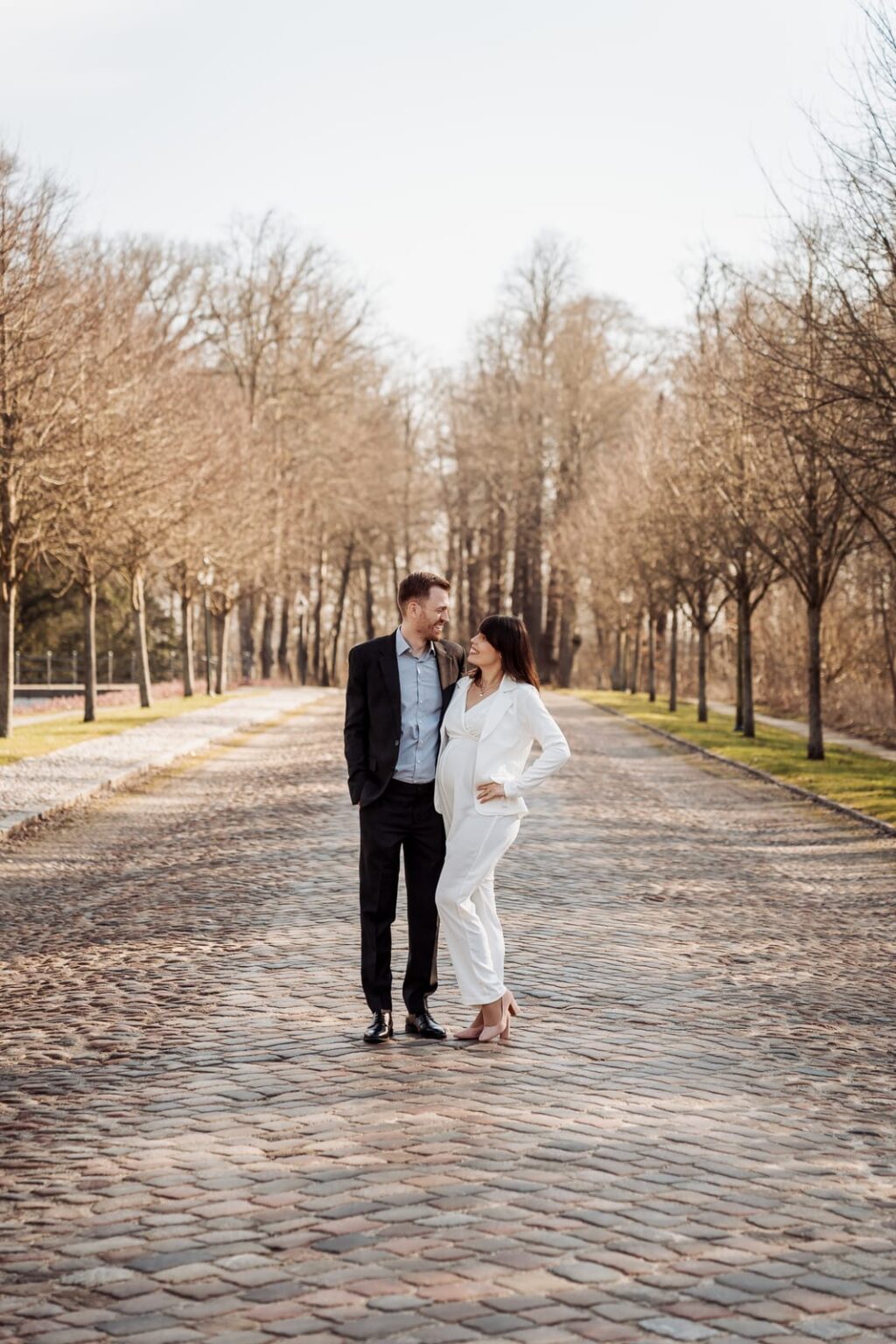 Bride and groom standing far down a tree lined cobbled avenue in Tønder, lit by low evening sun.