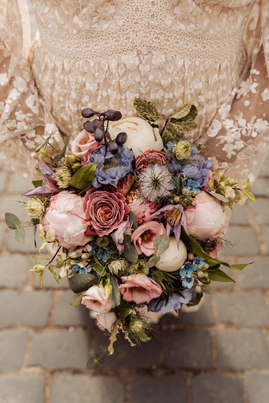 Bouquet of pink and blue flowers held against a lace dress on the cobbles in Tønder
