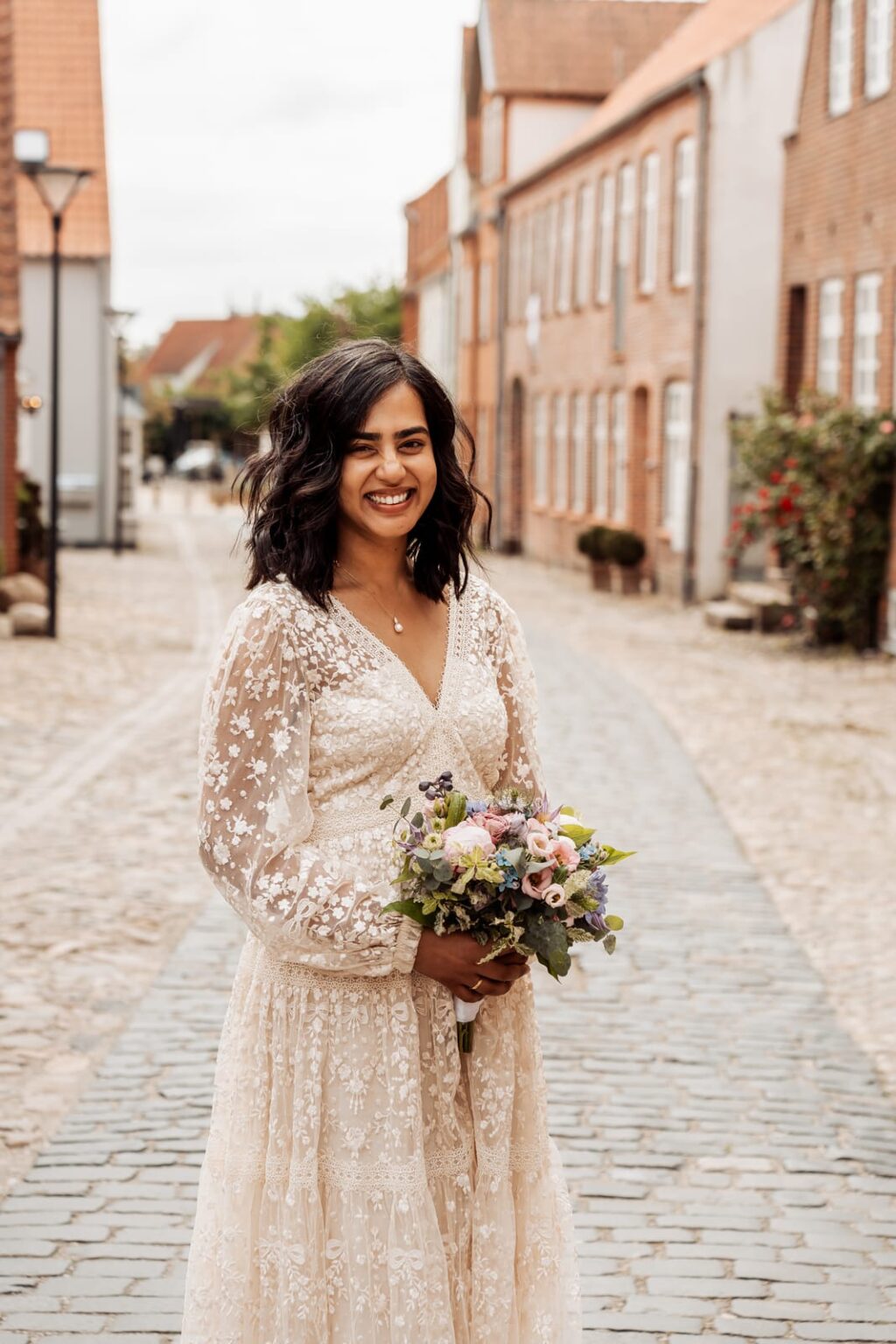 Bride standing with her bouquet in a cobbled street of red brick houses in Tønder.