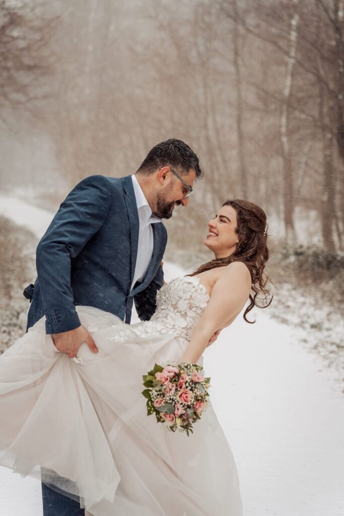 Bride lifts her dress as she walks through fresh snow with her groom in Aabenraa
