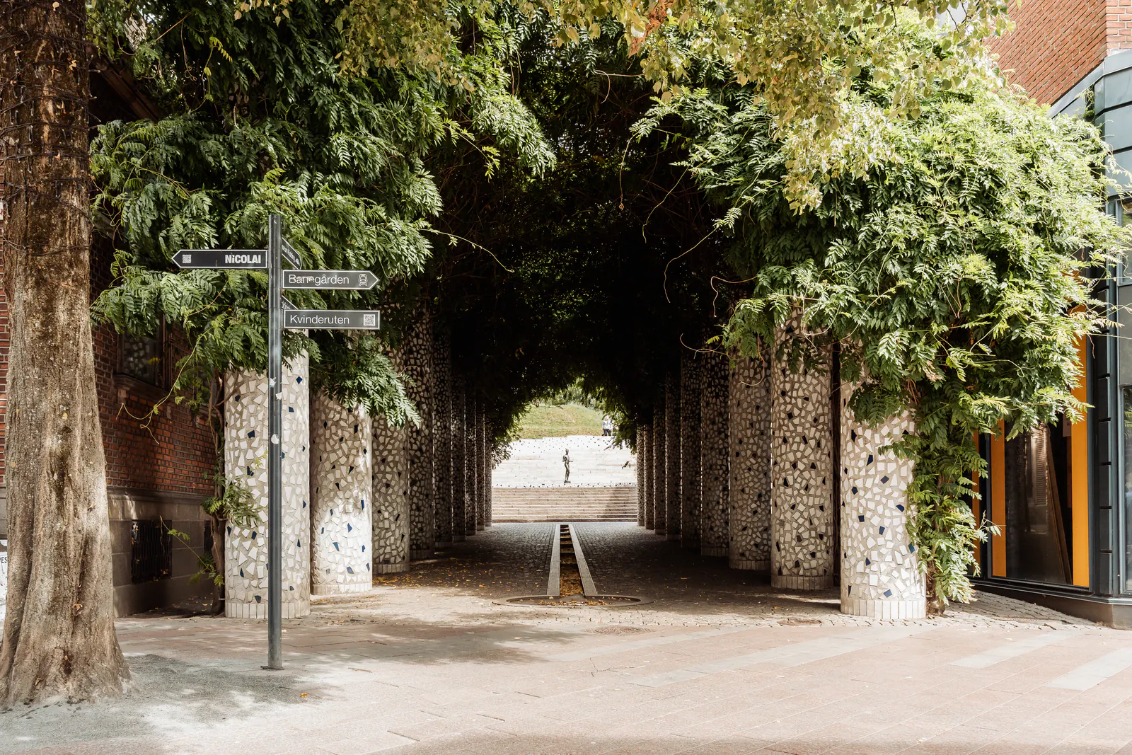 Stone mosaic pillars carrying a canopy of green over Jernbanegade in Kolding