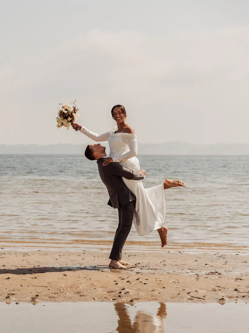 Groom lifting his bride on the beach in Aabenraa, her bouquet held high
